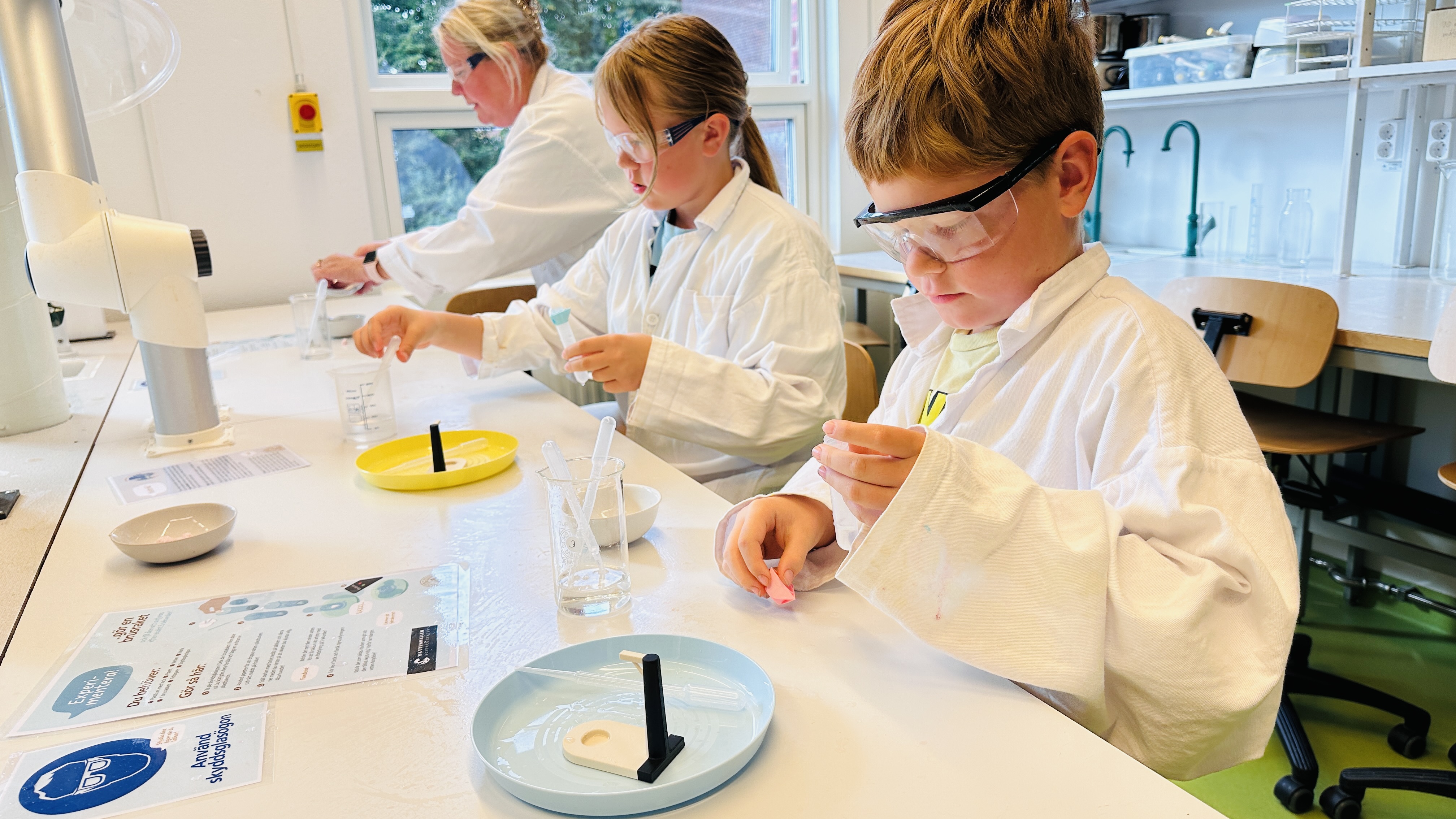 Två barn i labbrockar experimenterar i vårt kemilabb. Foto. 