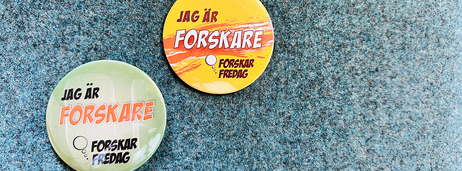 Två pins med texten "Jag är forskare" mot bakgrund i textil. Foto.